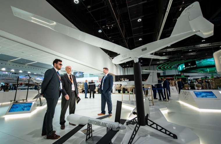 Visitors beside a large unmanned aircraft displayed inside an IDEX hall
