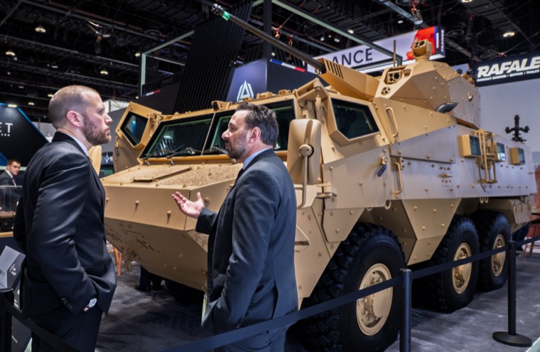 Two professionals speaking beside an armoured vehicle at IDEX